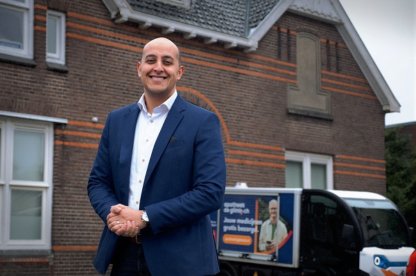 Foto van eigenaar Hamid Hamid Gongai van apotheek de Glimlach. Hij staat buiten en achter hem zie je een elektrische bestelbus